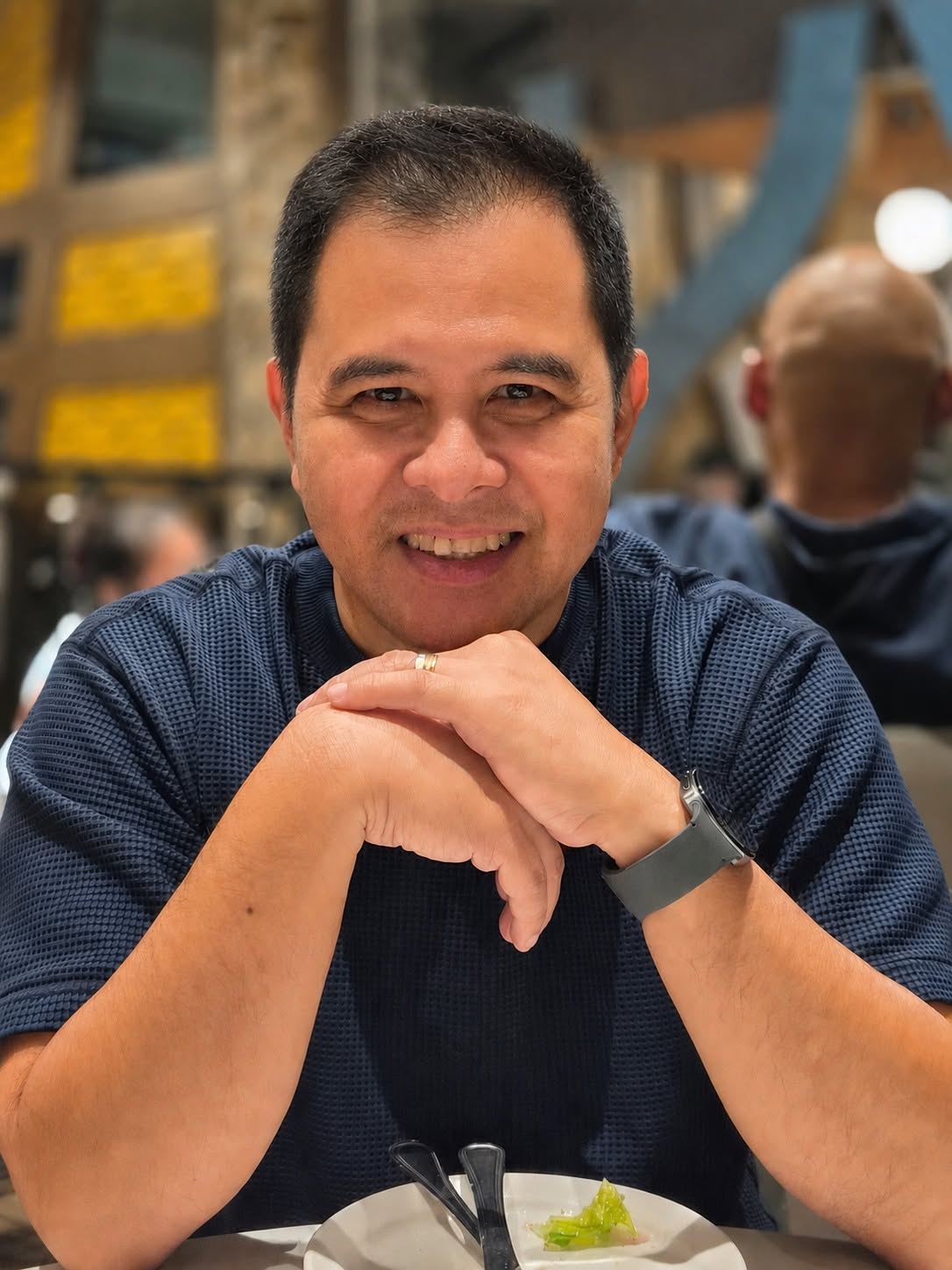 Arnold Gamboa, smiling with hands clasped at a café table